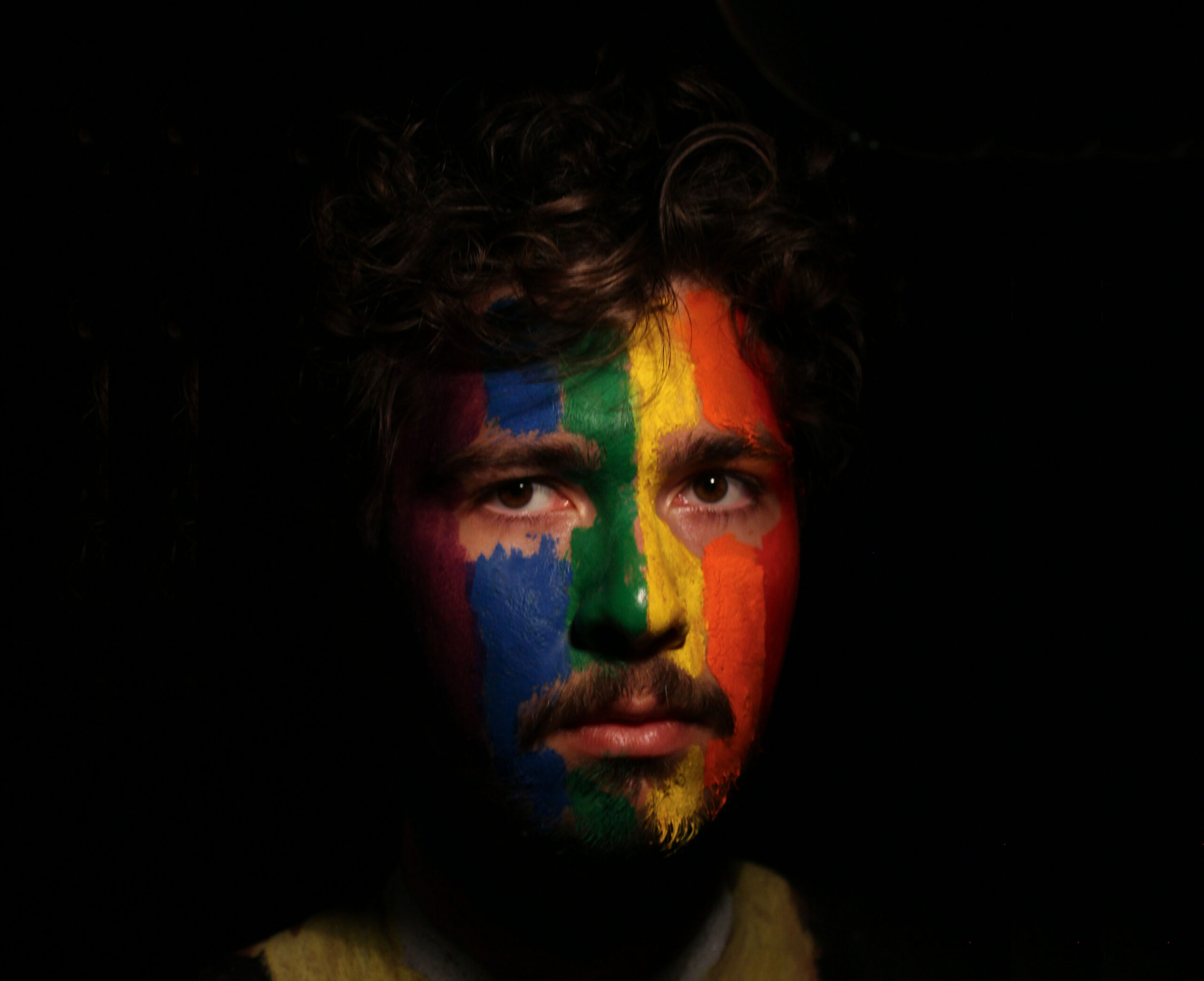 Portrait of young man face painted as lgbtq progress pride flag